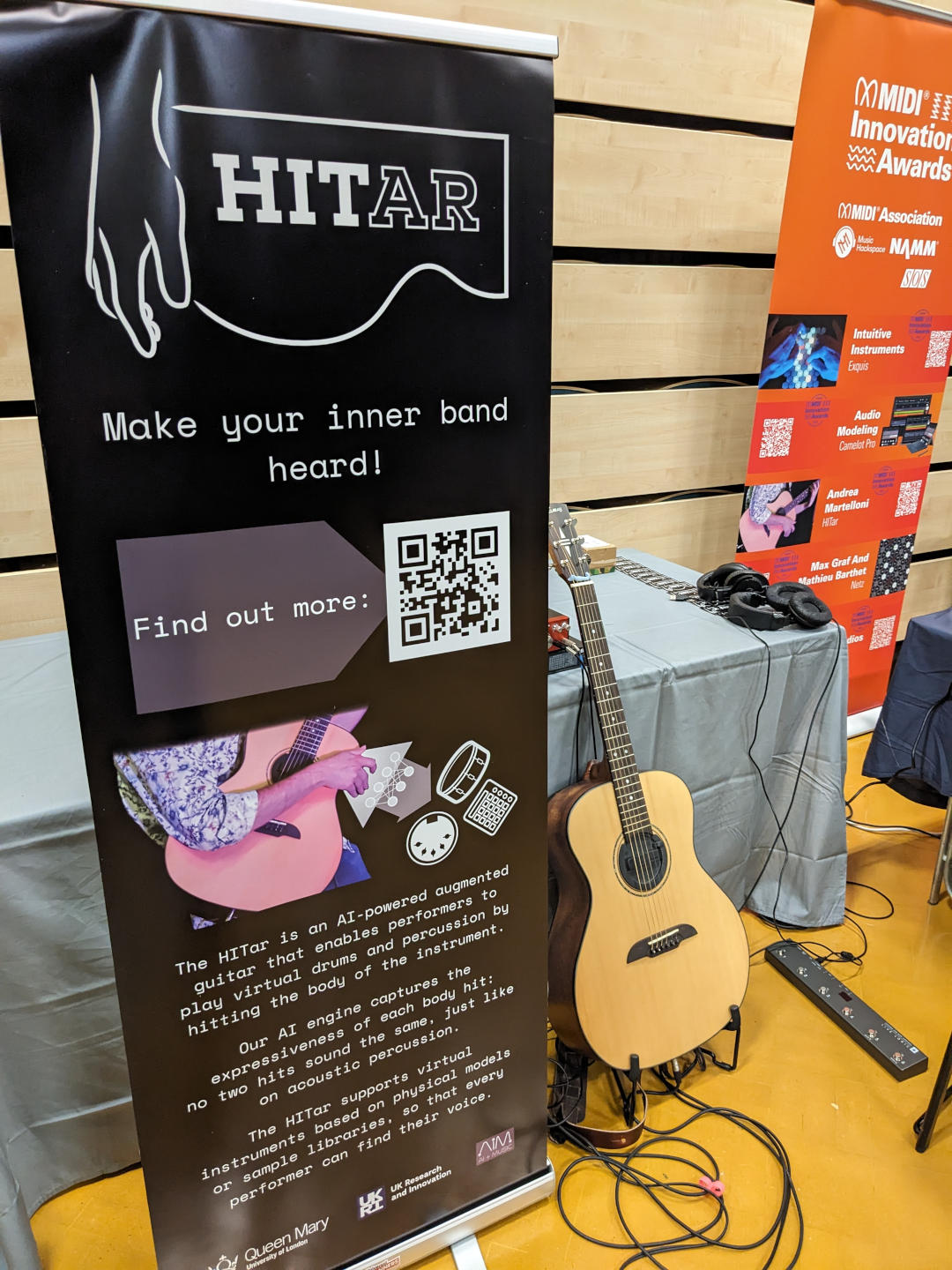 SynthFest2023 booth. Guitar on a stand with promotional banner.